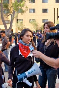 Student leader, Shahida Bawa, is interviewed by media sources that were covering the event. The protests were state-wide across all University of California campuses. However, the University of California Regents' meeting took place at the pictured campus, UCLA. While student leaders were explicit that the protest would remain non-violent and had communicated such with campus administration, police were deployed to the scene. Behind Bawa, several police officers are present wearing riot gear. Later, as the peaceful protests continued, campus police threatened students with tear gas, rubber pellets, and tasers if students refused to disperse. Some students were harmed and sought medical treatment. Photo courtesy of Asher Yap.