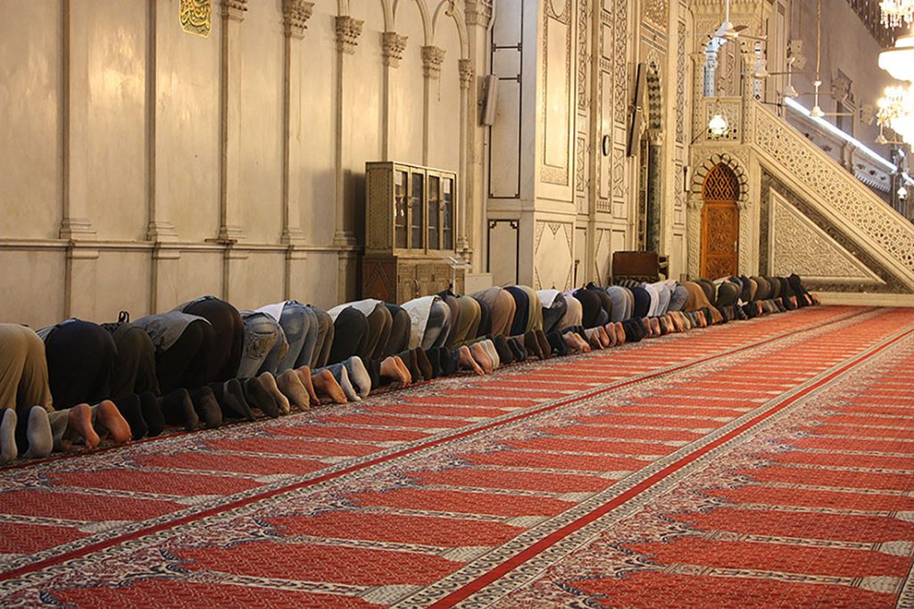 Figure 15.2 Universality of religious practice, such as these prayers at the The Umayyad Mosque in Damascus, can create bonds among people who would otherwise be strangers. Muslim people around the world pray five times each day while facing the direction of the Kaaba in Mecca (pictured in Section 15.2). Beyond the religious observance, such a unifying act can build a powerful sense of community. (Credit: Arian Zwegers/flickr).