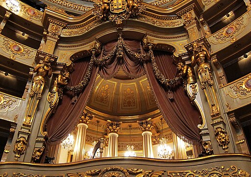 Extravagant theater box with columns, curtains, and gold pillars.