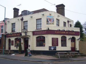 The Canterbury Tales Public House in Gillingham, England, a historic two storey building with two brick chimneys, two signs, and a painting of the Canterbury pilgrims on the front.