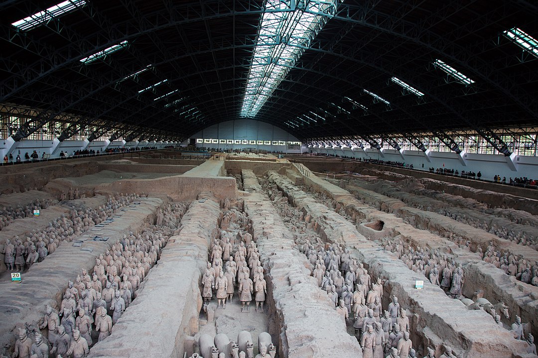 Large room with dug trenches, filled with hundreds of sculptures of men in armor