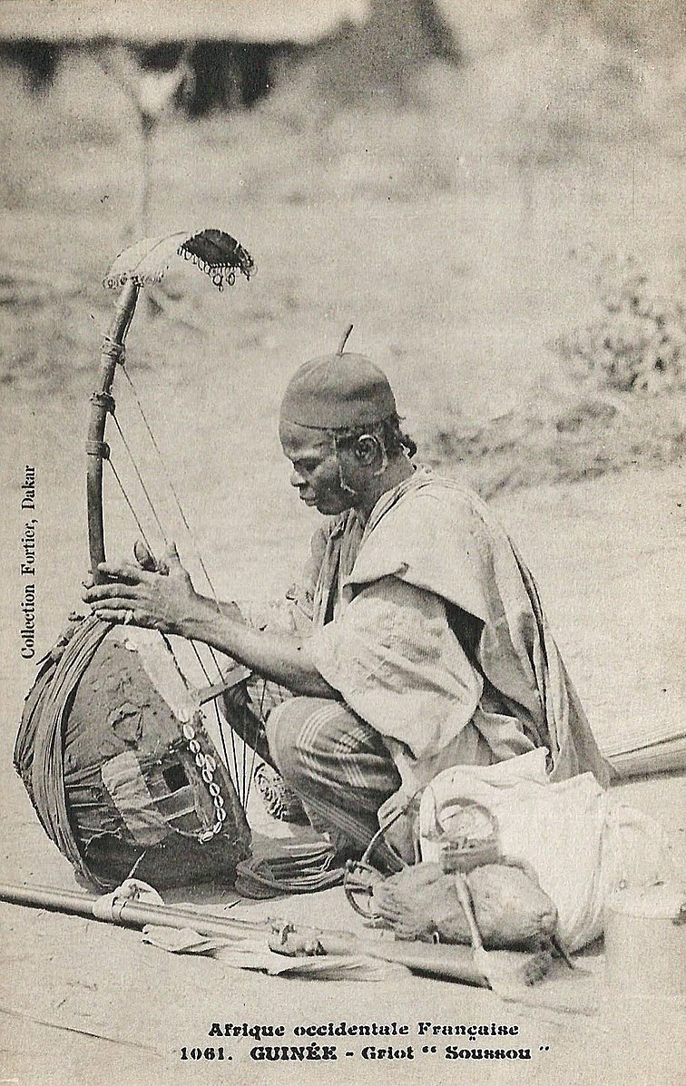 Man holding onto and surrounded by traditional items with heading indicating taken in French controlled African region of Guinee.