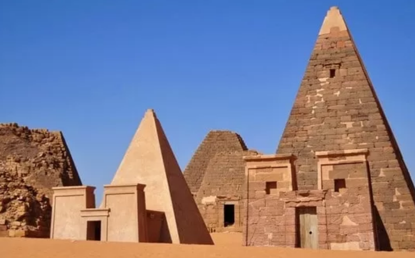 Collection of ancient pyramids with other ancient structures nearby, set in the desert.