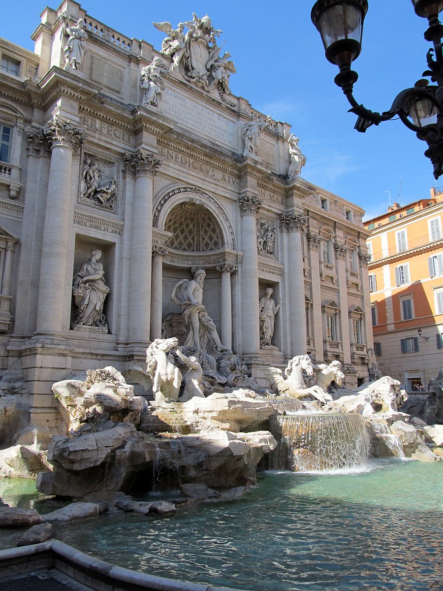 Large building surrounded by marble statues and a massive fountain with several marble statues