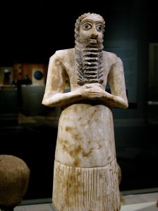 Carving of standing man with long beard holding hands clasped together in front of of his torso