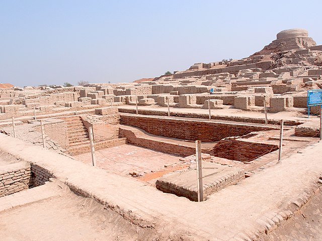 Ruins of large mud brick complex with large swimming pool in forefront, and large structure on a hill in background