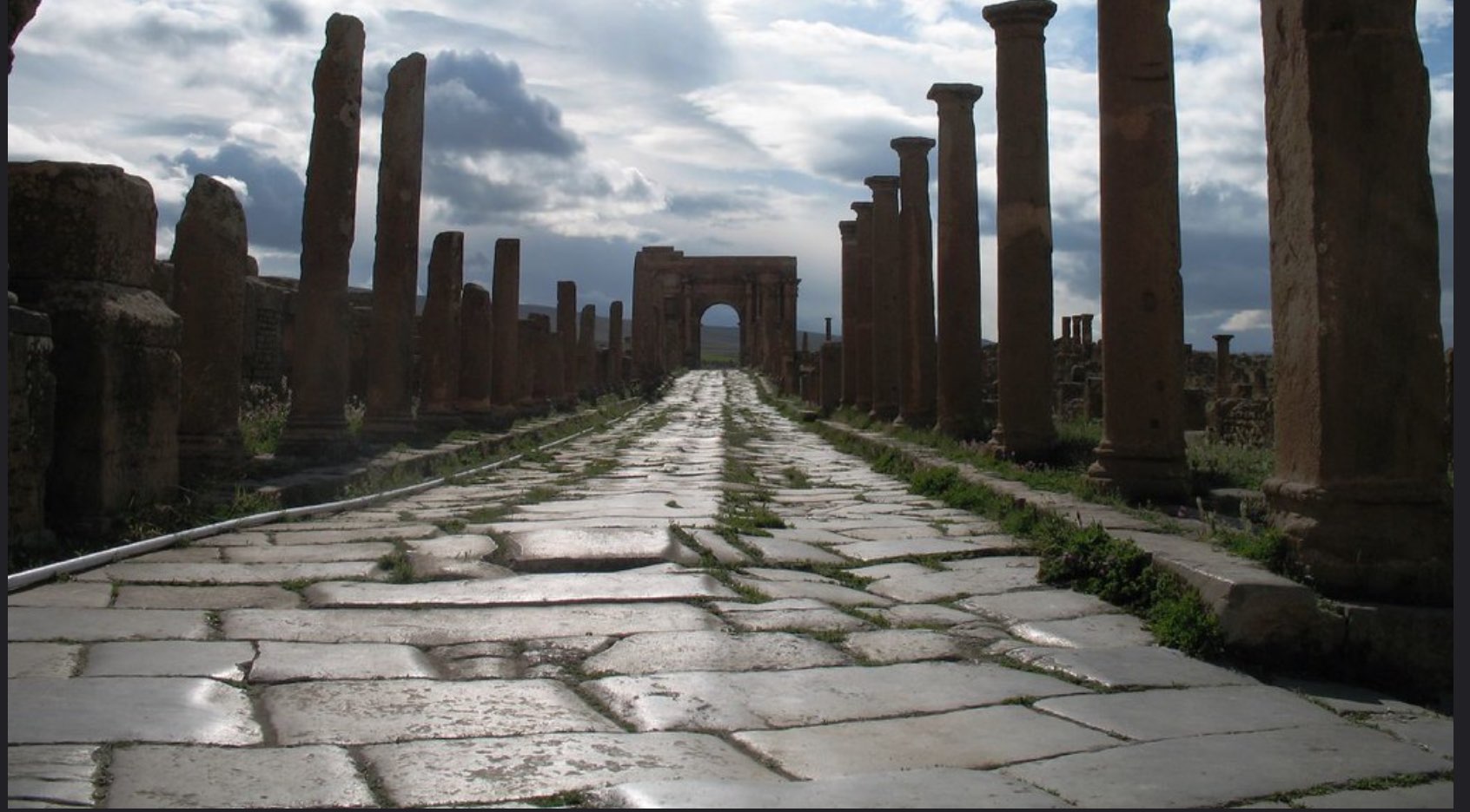 Ruins of pillars and walls with ancient stone road at the center