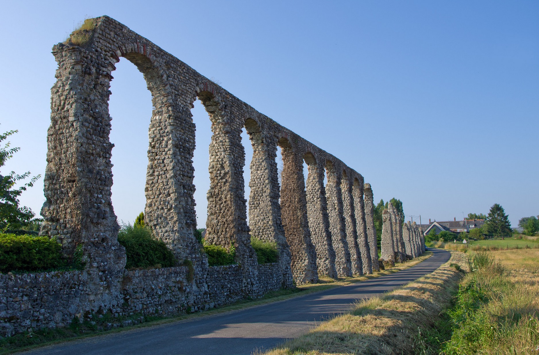 Remnant of ancient aqueduct with large stone arches alongside a modern road