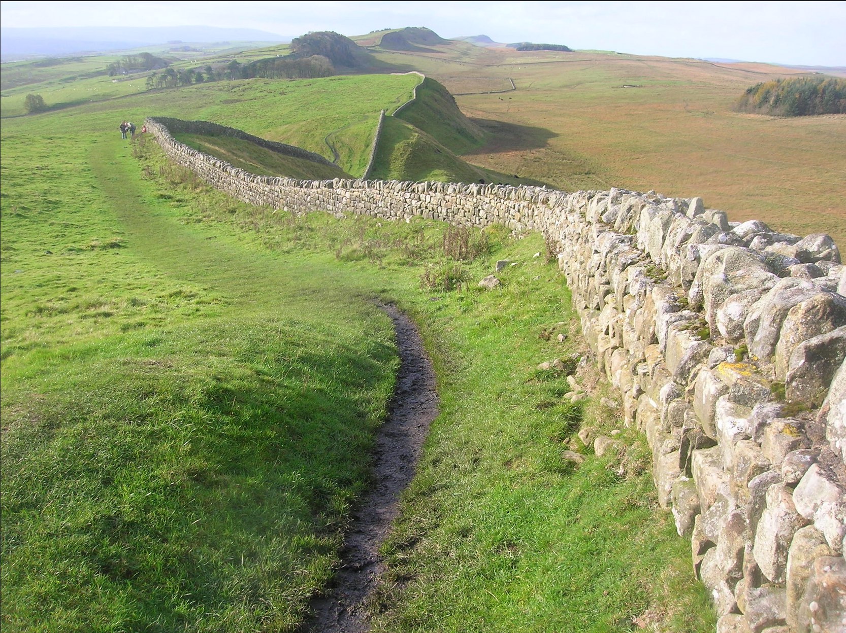 long stretch of stone built Hadrians wall with surrounding countrysite