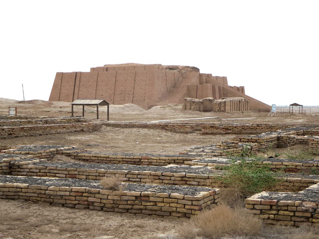 Massive structure with ramps in background, with stone wall ruins in the forefront