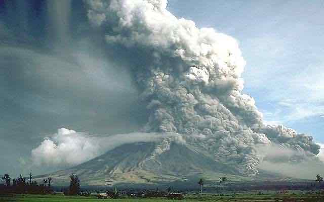 Volcano with massive cloud of ash rising above and flowing down the side