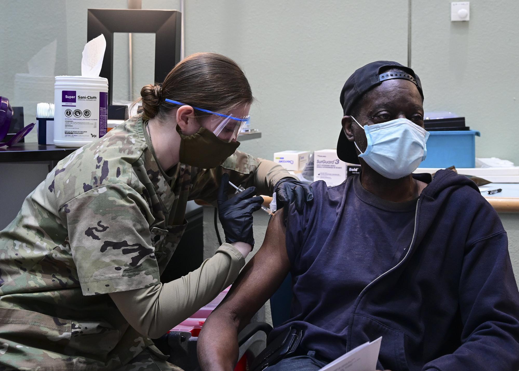 A healthcare specialist in camouflage uniform gives a veteran an injection in the arm