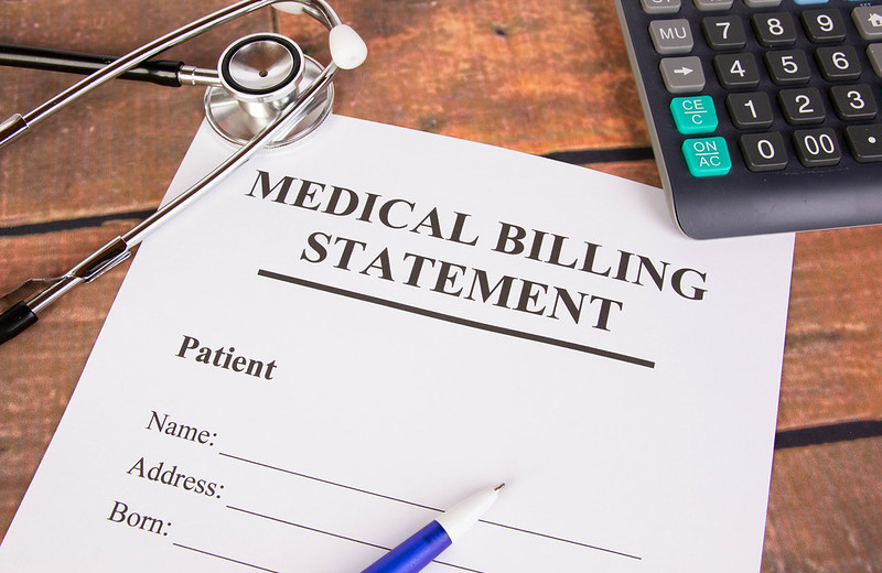 laying on a desk is a paper titled “medical billing statement” with a stethoscope and office supplies scattered around it.