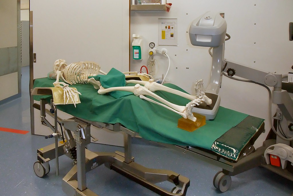 A fake human skeleton laying down with an x-ray machine taking an image of the foot.