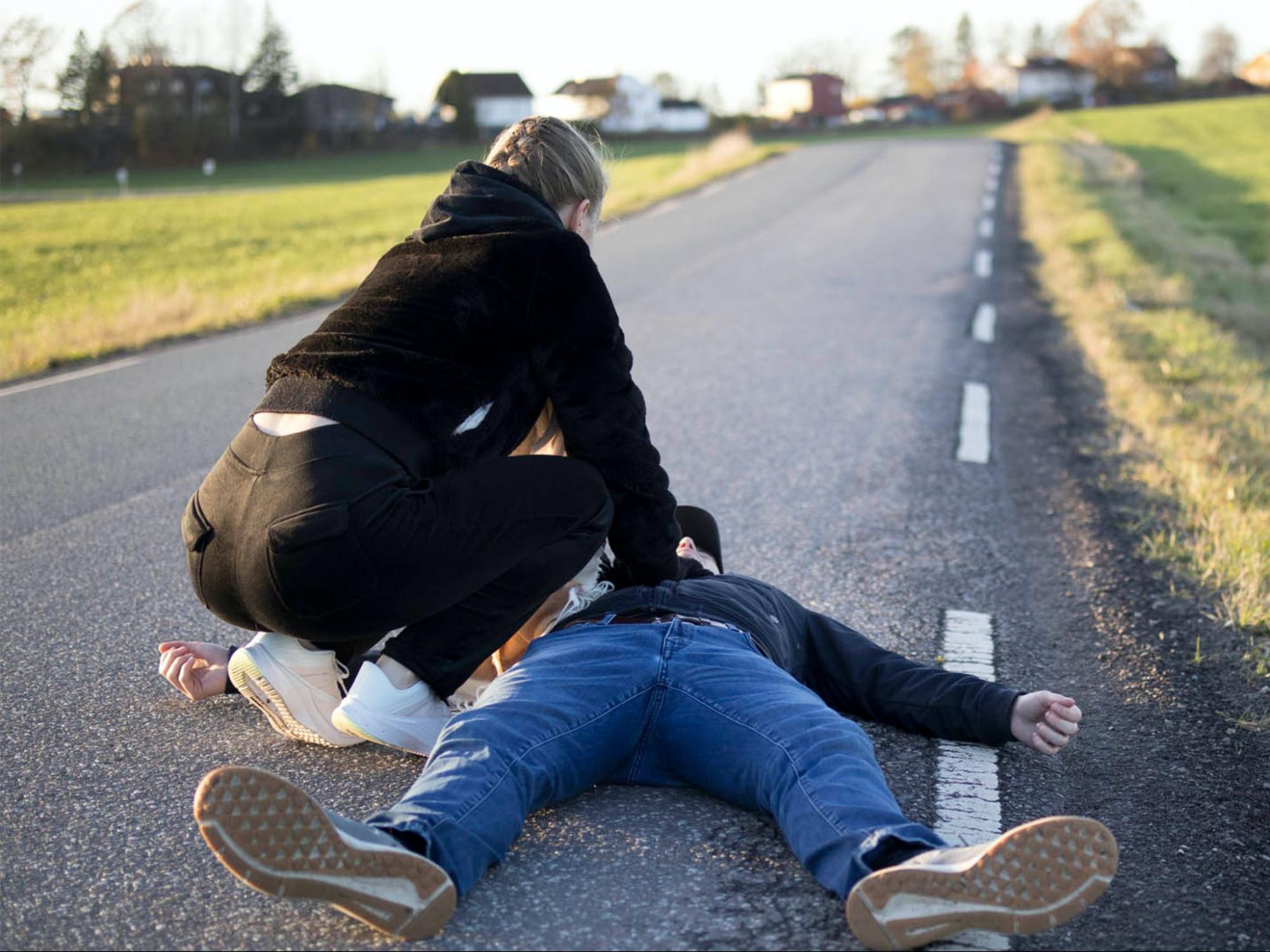 A man is lying on the ground while a woman provides chest compressions