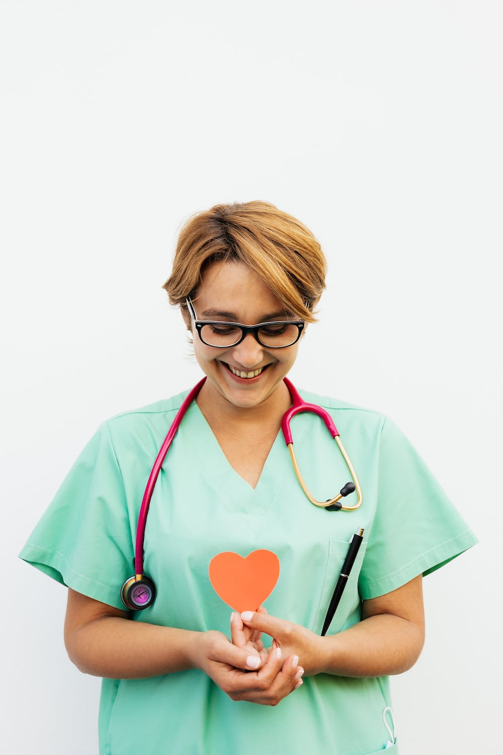 A young woman in a green top holds a small orange paper heart