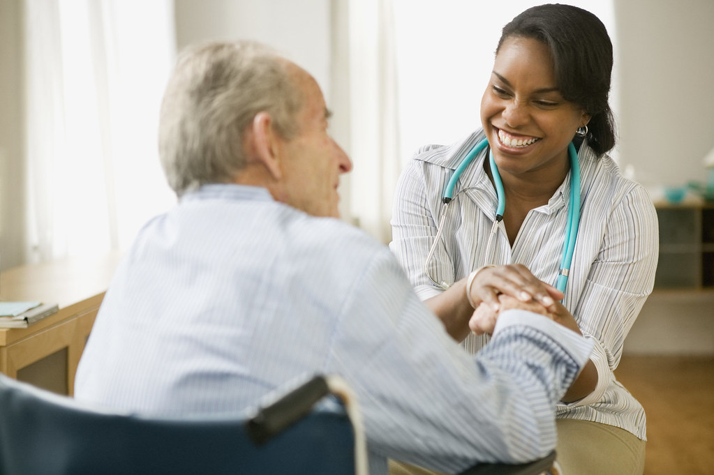 Healthcare professional sitting with elderly holding his hand smiling