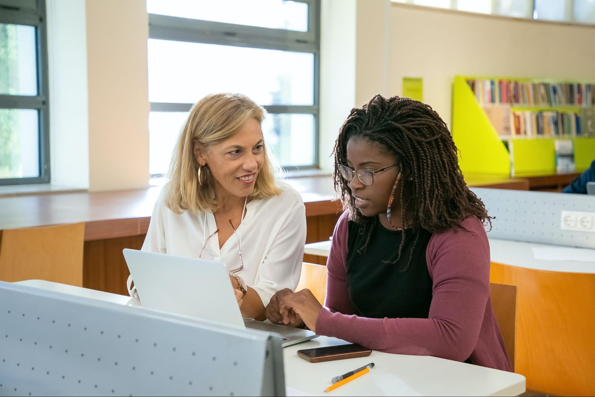 Two women sitting at a table while looking at a laptop computer