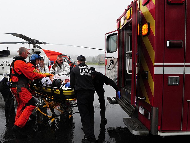 Medical personnel loading a patient into an ambulance next to a rescue helicopter