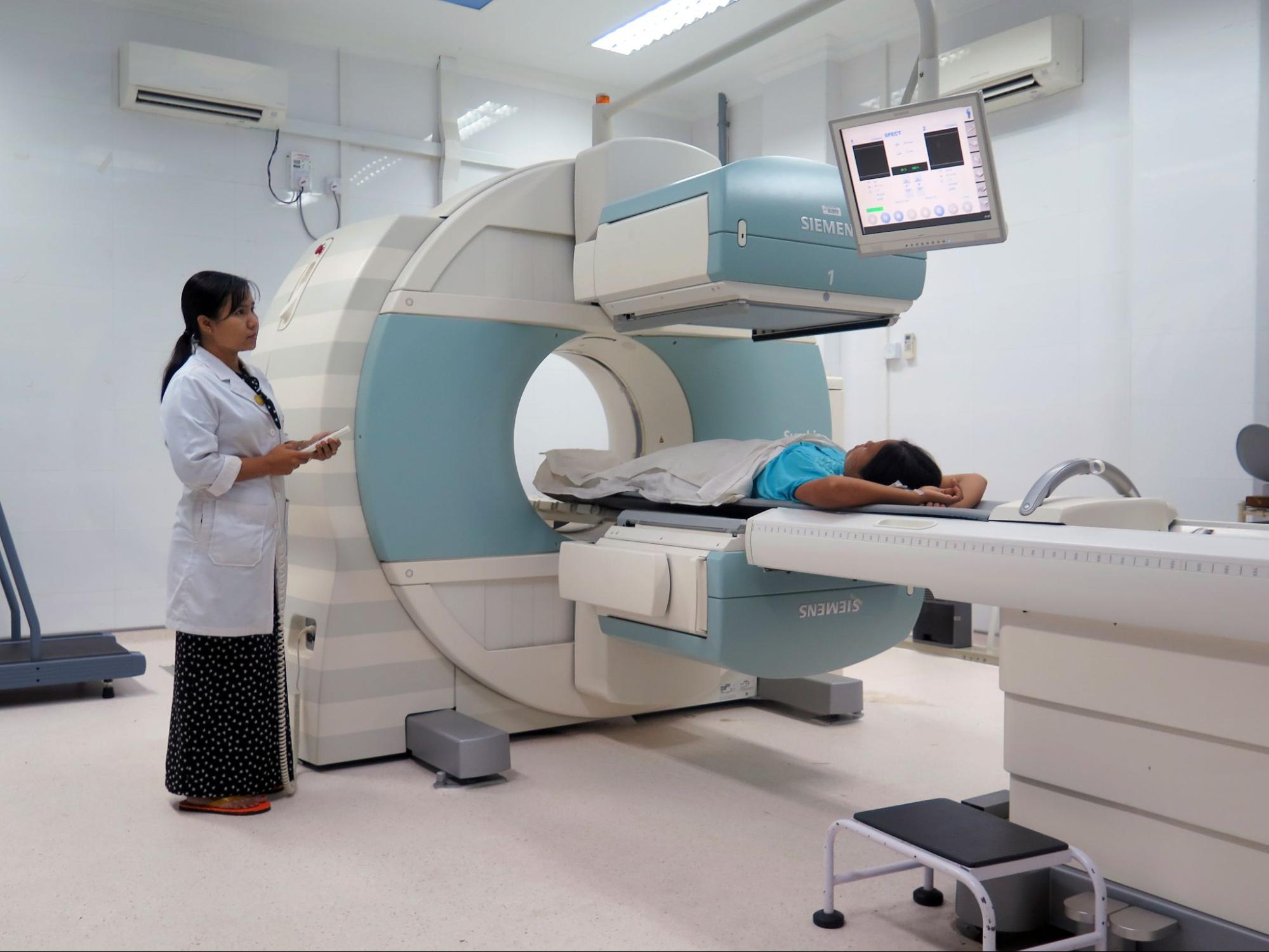 A CT technician operating the CT equipment with a patient lying on their back.