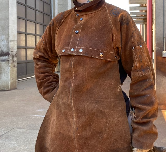 The torso of a person wearing a set of leather button-up welding sleeves and snap-on bib.