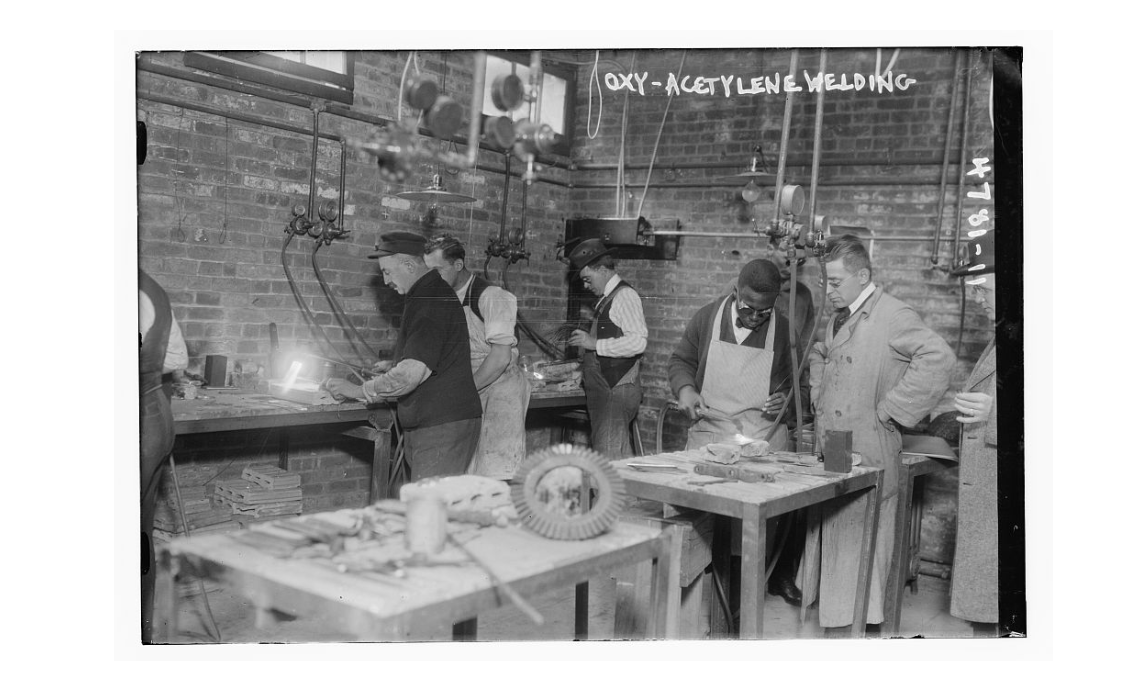 A historical photograph of five men of different racial backgrounds in a workshop, welding. The top right of the picture is labeled oxy-acetylene welding.