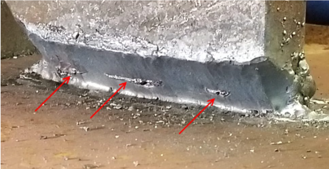 Slag Inclusions shown on a weld bead that has been cut into, to expose the slag. Three rough spots appear on the edge of a piece of metal. Three red areas point to the rough spots.