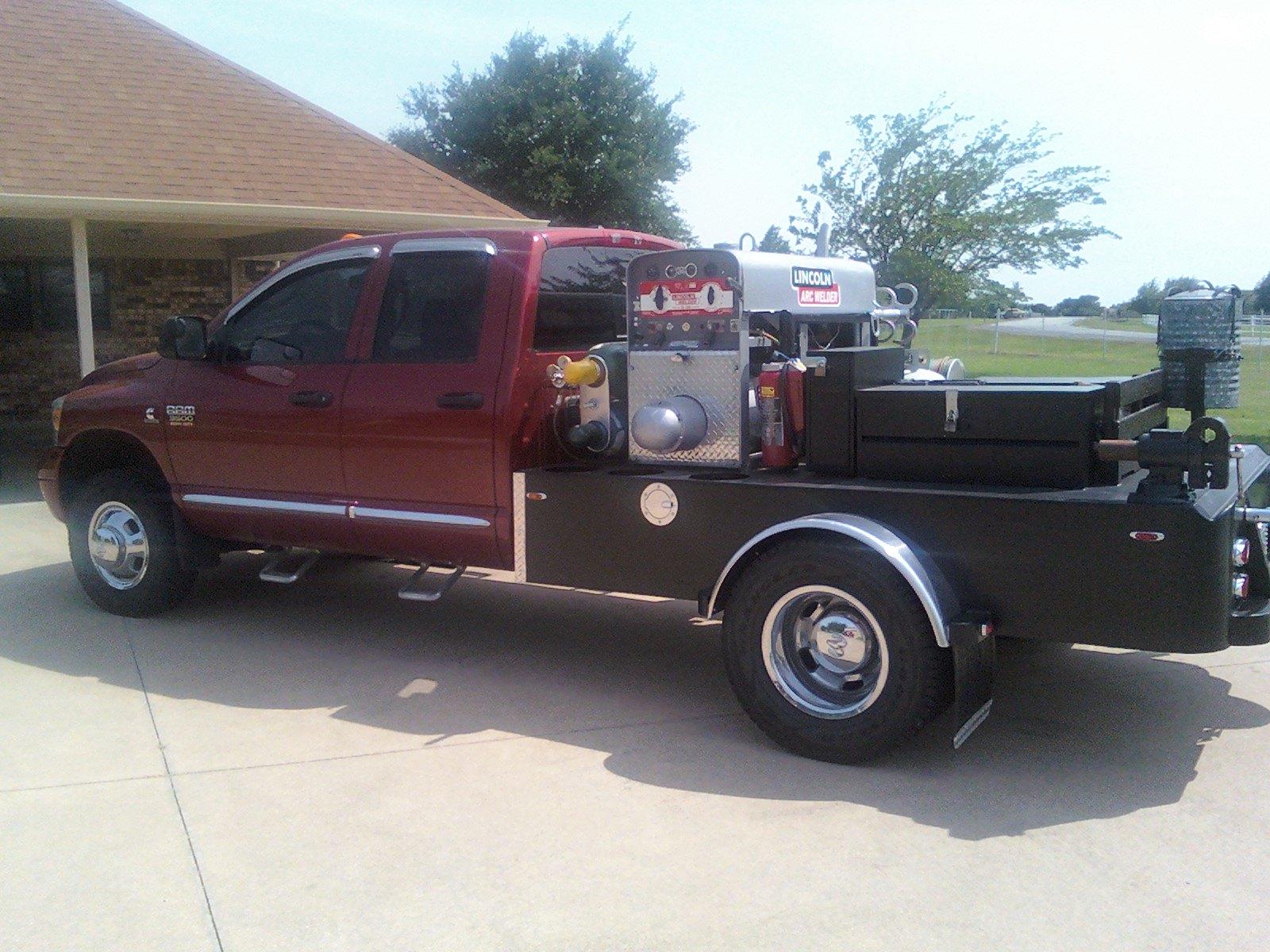 A pickup truck with a flatbed has a large generator welder and other equipment mounted on the rear.