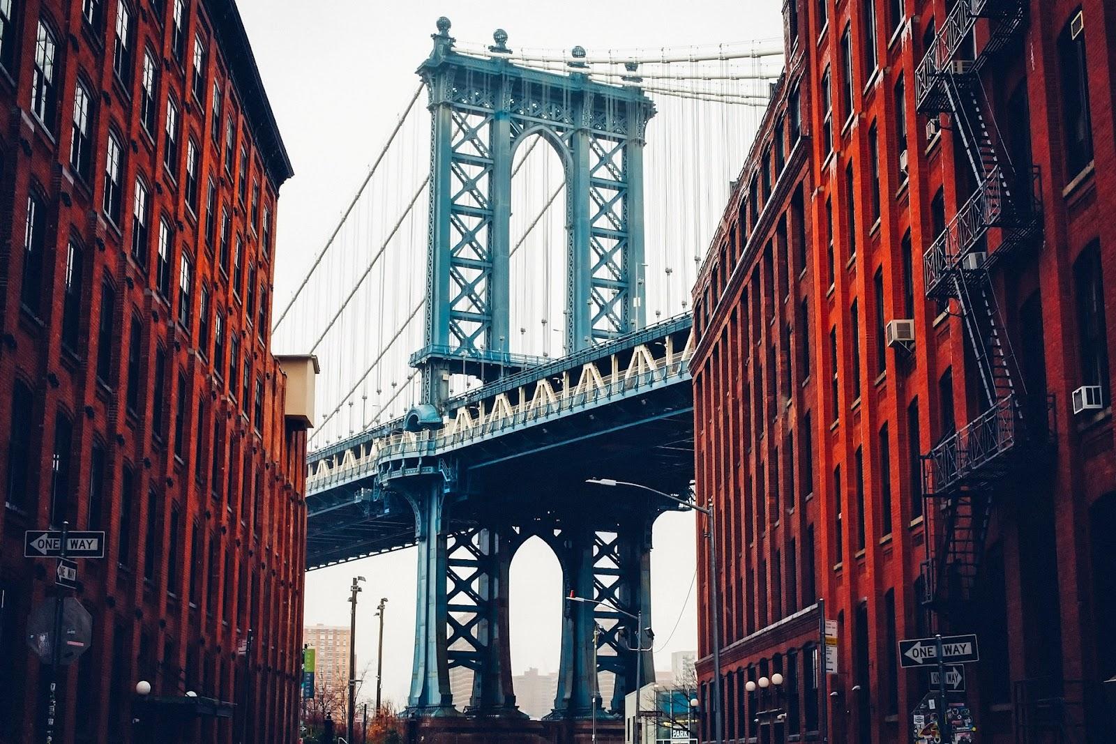 A city scene of buildings with a suspension bridge in the background.