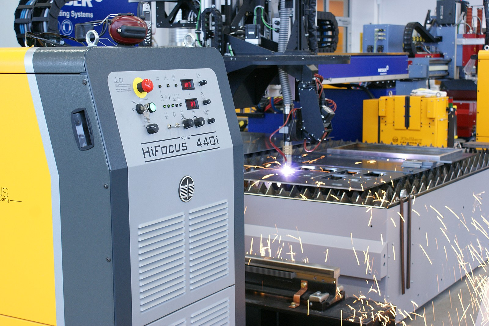 In a shop, a CNC plasma table, where a robotic arm is holding a plasma torch as it cuts into a piece of metal laid out on a table.