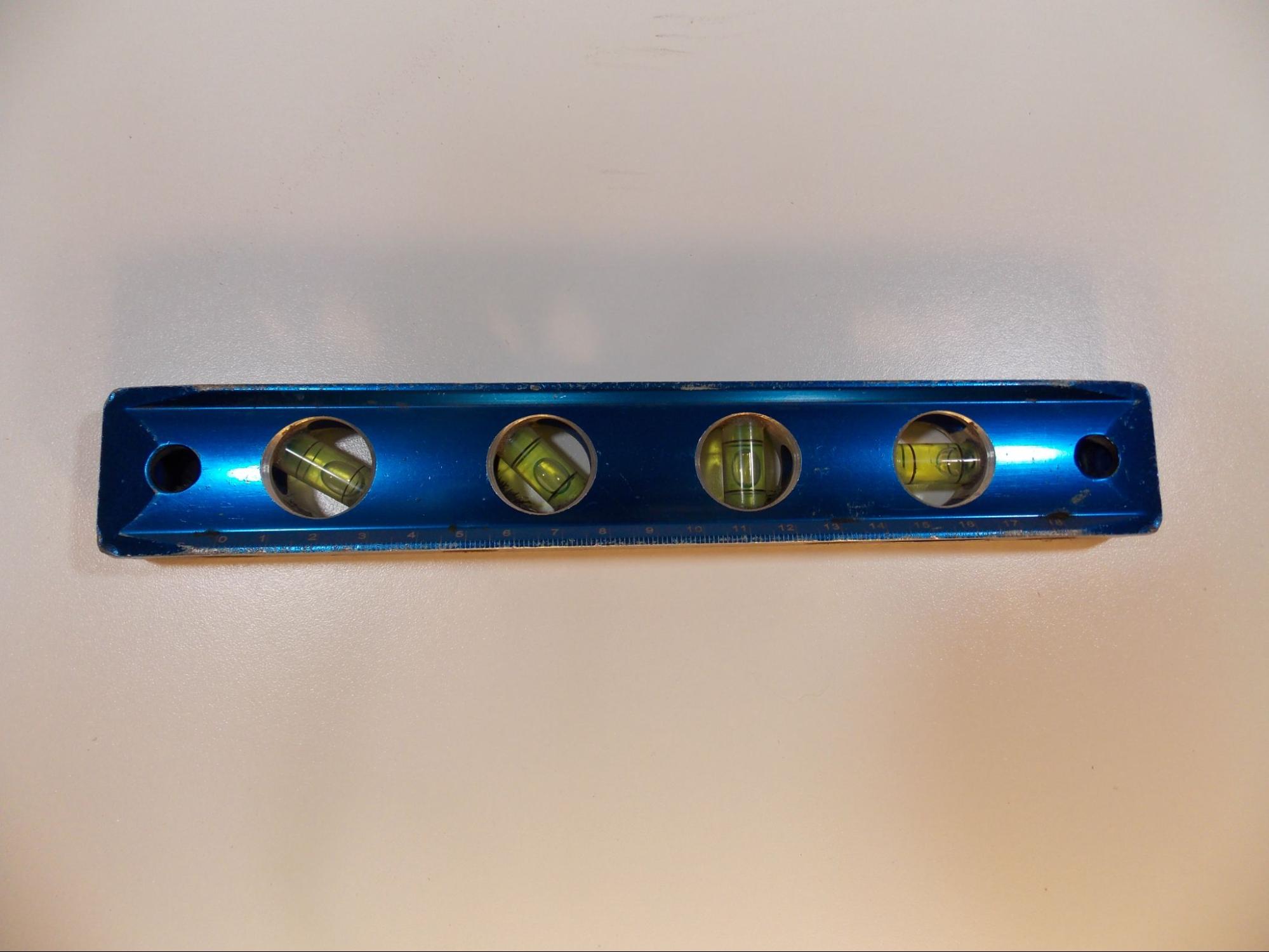 A blue torpedo level with four cutaways that hold plastic tubes containing bright yellow liquid with a single air bubble in each. Marks on the tubes indicate where the bubbles should rest when the level is in the desired position to indicate four different angles with reference to the edge of the tool: from left to right they are 30 degrees, 45 degrees, 90 degrees (vertical), and 0 degrees (horizontal).