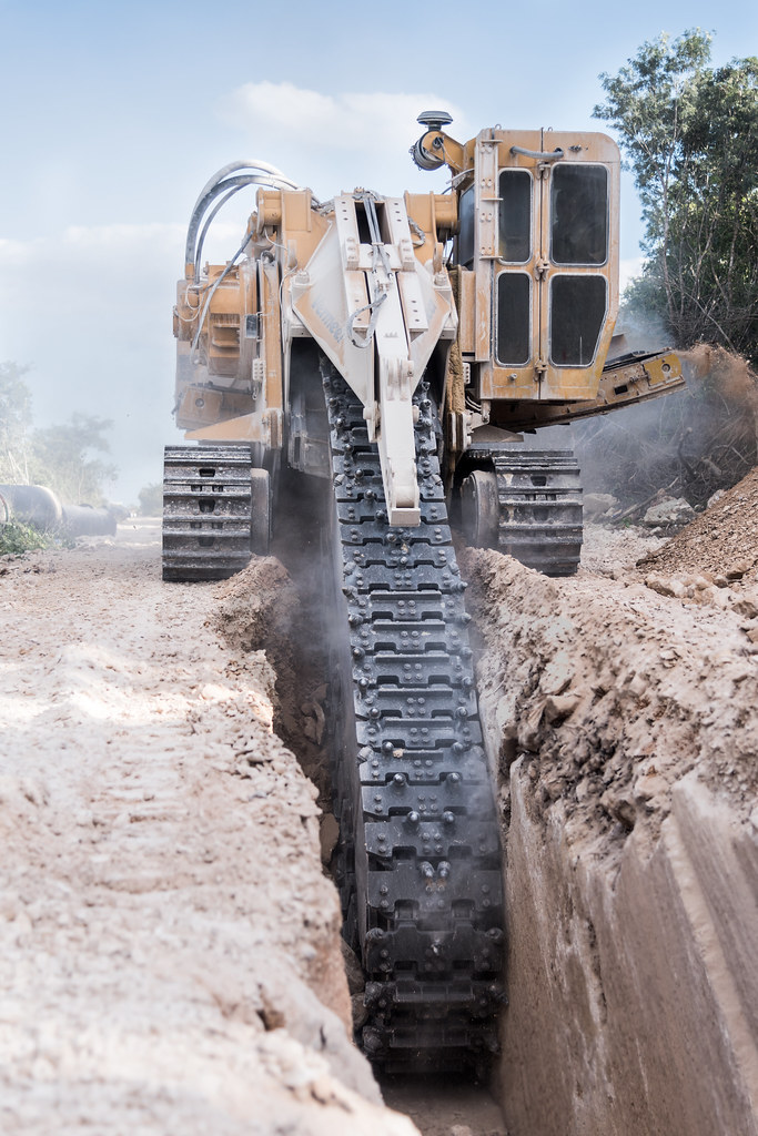 A trenching machine on crawler treads digs a trench.