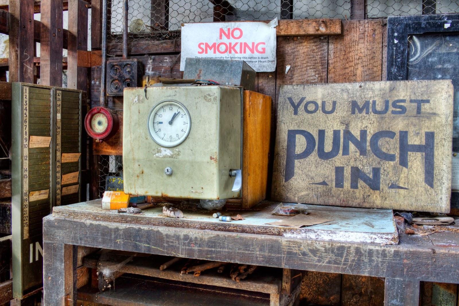 An old-style time clock is on a table next to a sign that reads “you must punch in.”