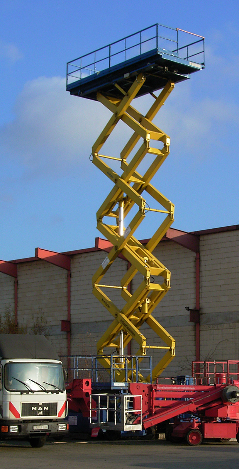 A large scissor lift outside of a building is extended up into the air, high above the roof of the building.