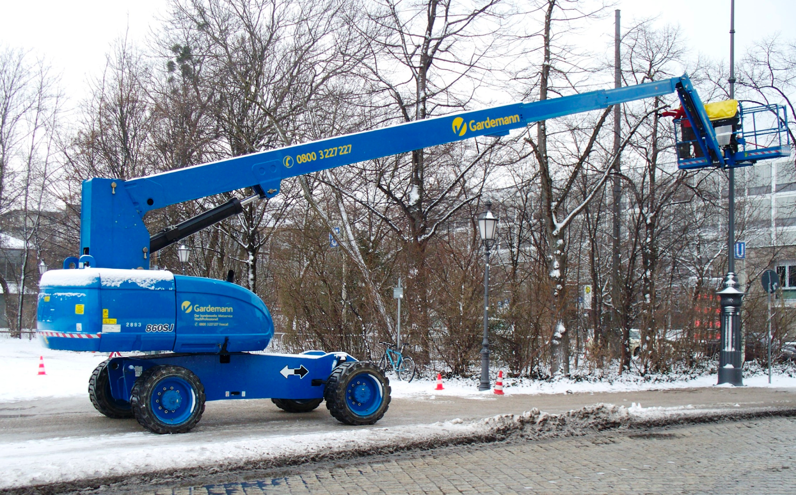 A large blue boom lift parked outside on a snowy sidewalk.