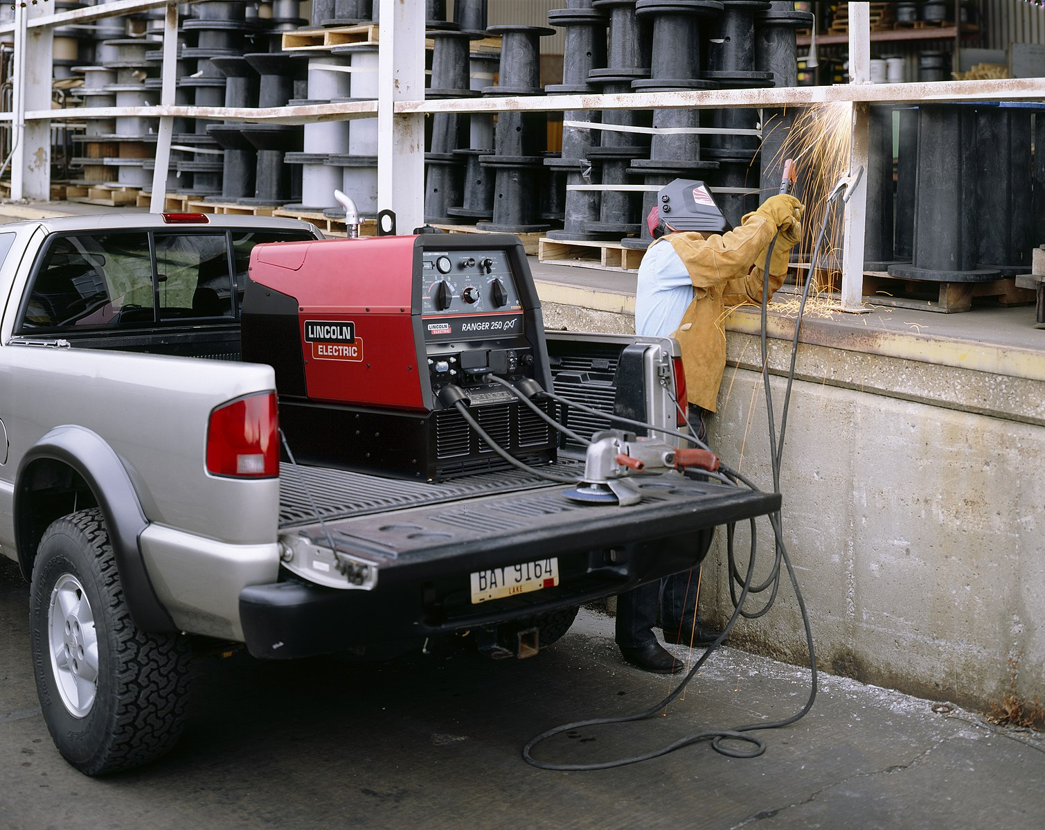 A welder repairs a handrail with SMAW, powered by an engine-driven welding machine in the back of his pickup truck.