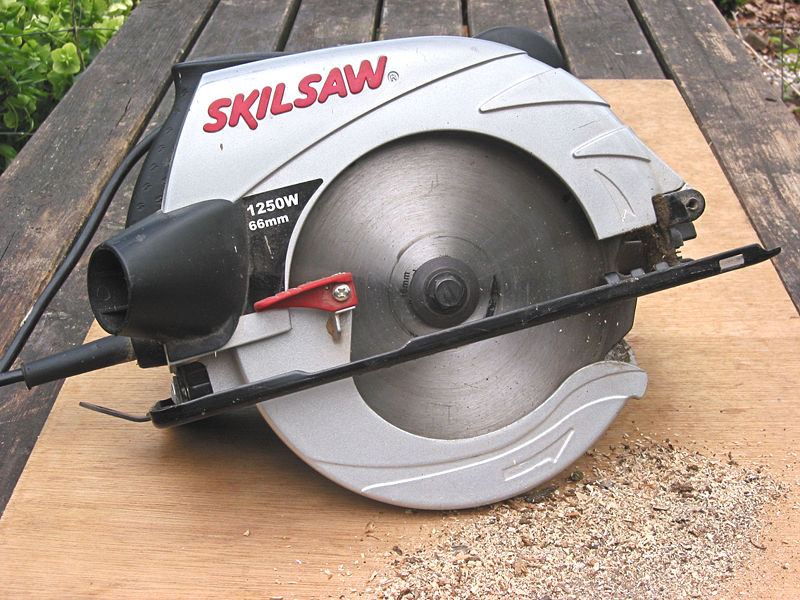 A common circular saw. This power tool has a large rotating circular blade surrounded by a protective guard. On the back side of the guard is the handle to hold the saw. The tool has a flat metal table mounted perpendicular to the saw blade that can be raised or lowered to establish the depth of cut. At the back of the guard is a small chute to eject saw dust.