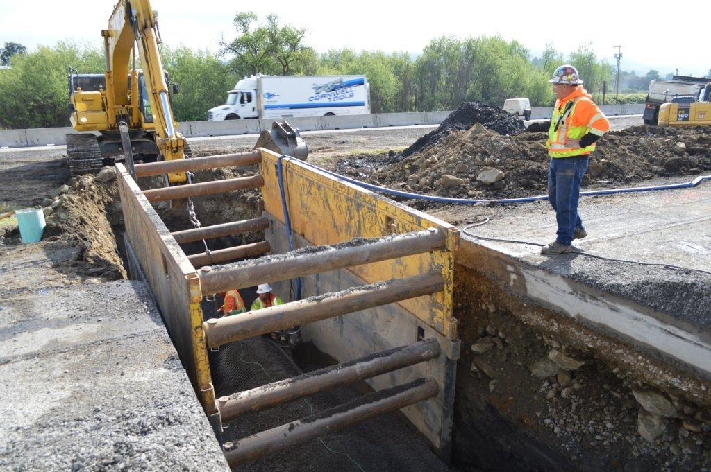 A pair of steel plates separated by pipes is used in a large trench to protect workers in the trench from cave-in.