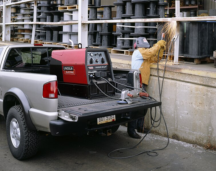 A welder performs SMAW on some railing using an engine-driven power source.