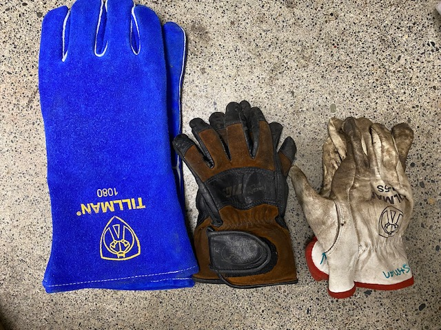 Three different leather-type gloves, each providing a different amount of protection. A blue pair with a long cuff labeled Tillman 1080, a brown pair, and a white pair with red trim.