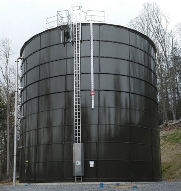 A large cylindrical shaped steel water tank with a pipe on the left side and a ladder going up the front of the tower.