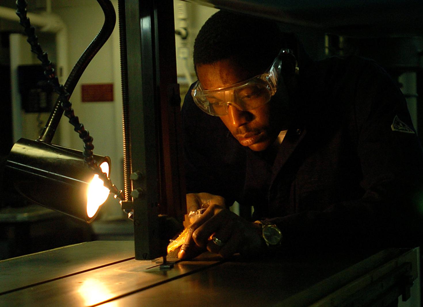 A fabricator uses a vertical band saw to cut an intricate part.