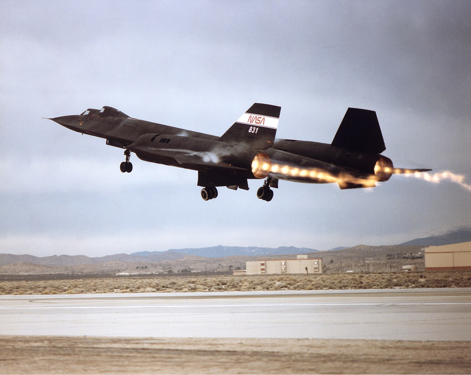 An SR-71 Blackbird Aircraft taking off. The aircraft is black and has NASA 831 printed on a fin that rises midway up the back of the craft.