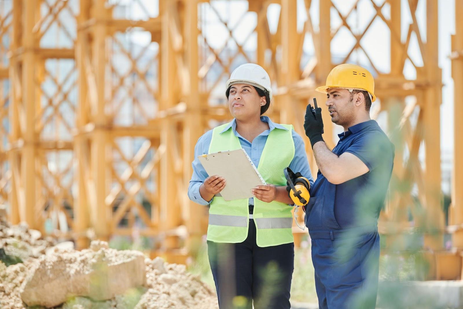 A man and a woman in hard hats on a construction site.