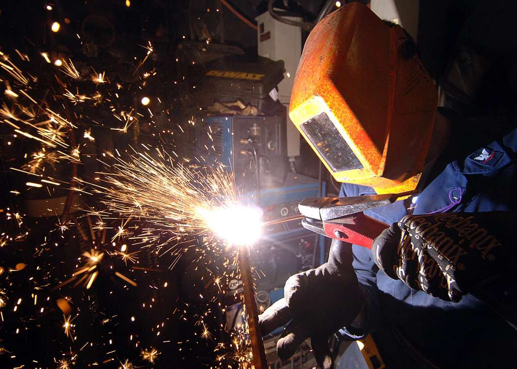 A person in an orange welding hood and blue coveralls uses the CAC-A process in the horizontal position.