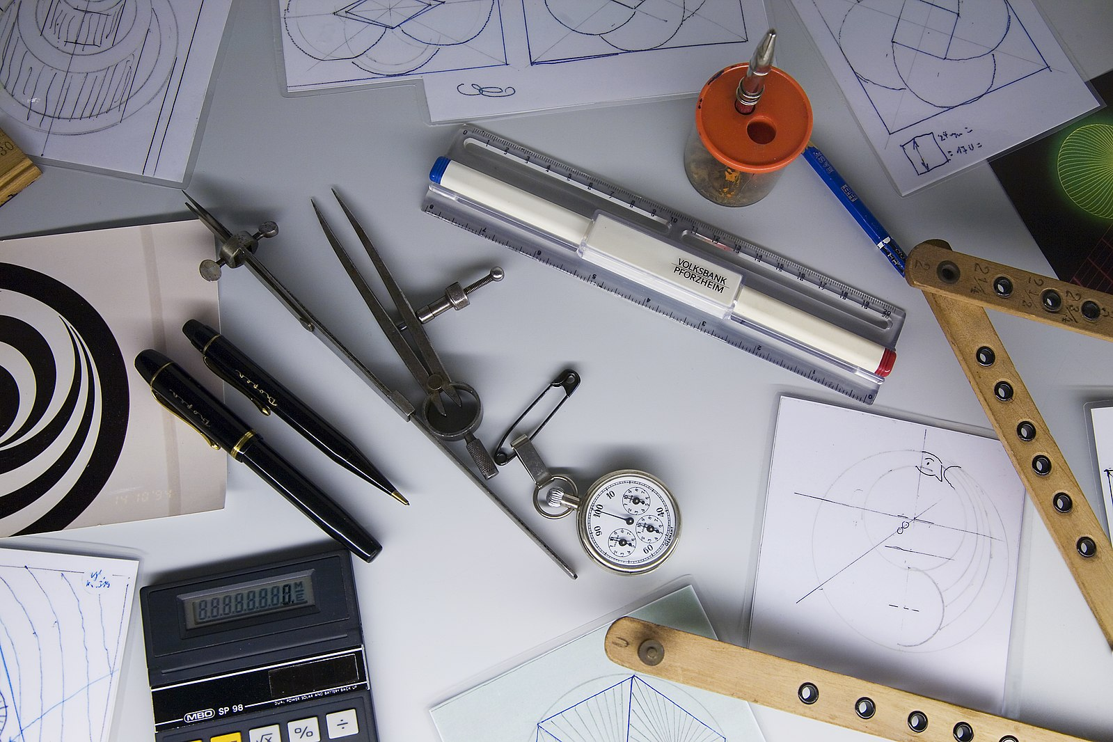 A desk strewn with rulers, pens, compasses, and other layout tools, along with patterns that are being worked out.