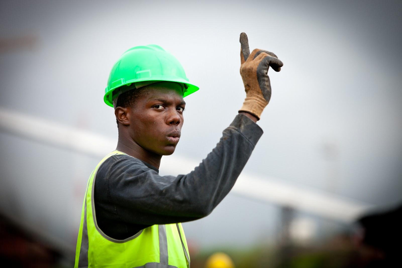 A man in a green hard hat holds up a finger as if to say, “Wait a minute!”