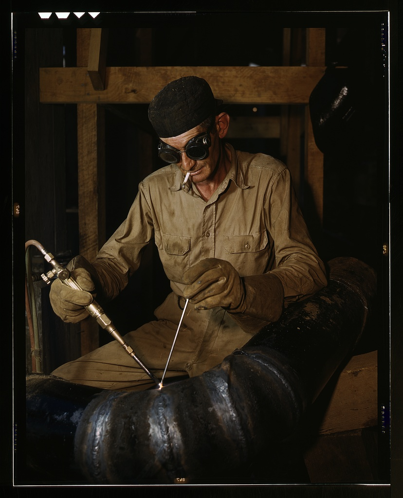 Welder sitting while smoking and Oxy-Fuel Welding pieces of spiral piping together.