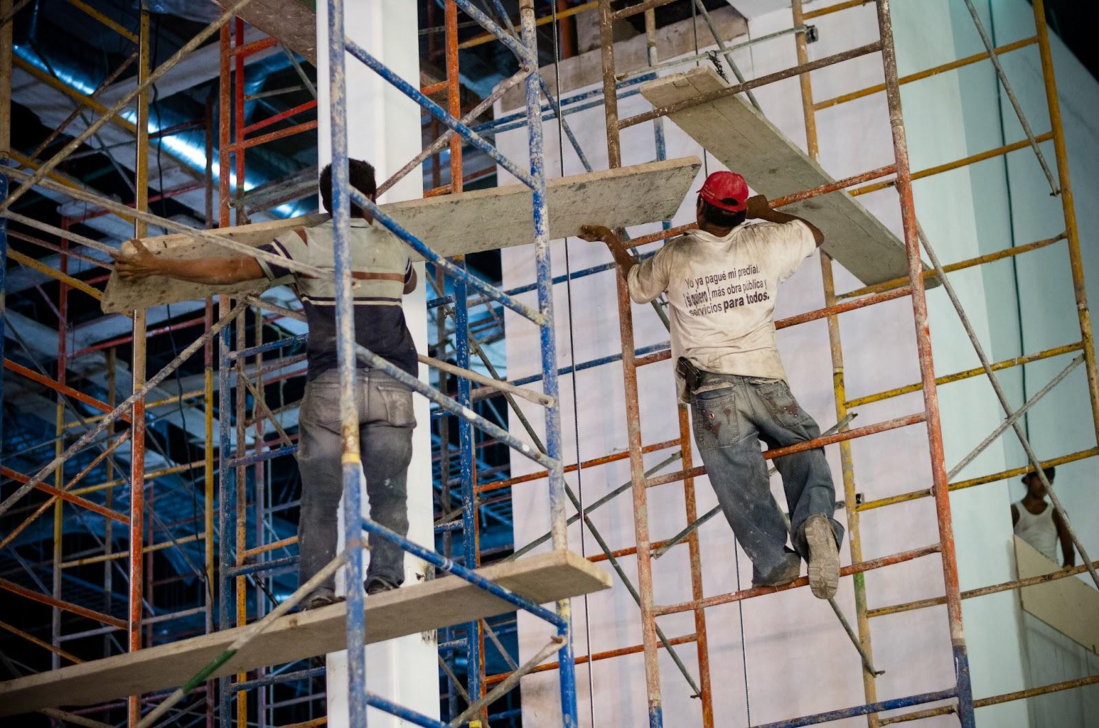 Two workers are erecting scaffolding without wearing fall protection or other PPE.