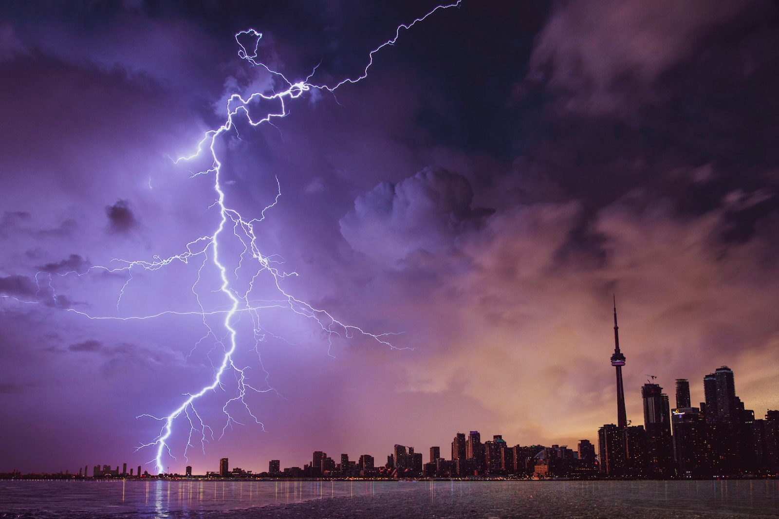 A landscape of a city with lightning arcing through a purple and cloudy sky.